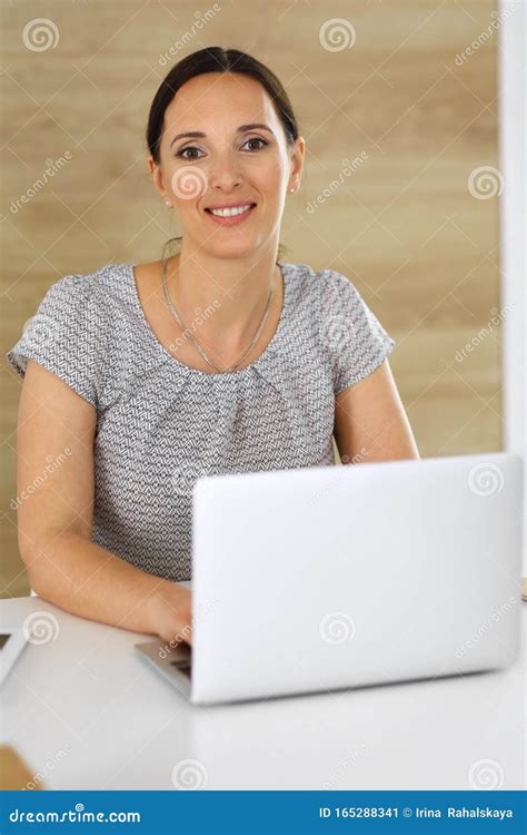 cheerful smiling business woman working with laptop computer while sitting at the desk in modern