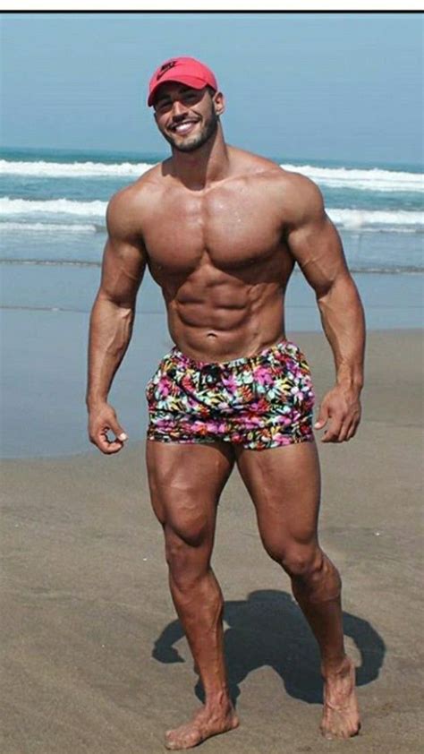 A Man Standing On Top Of A Beach Next To The Ocean Wearing Swim Trunks