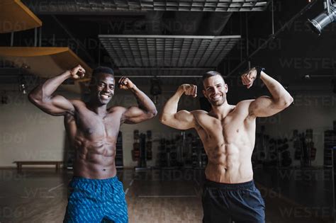 Happy Male Sports People Flexing Muscles In Gym Stock Photo