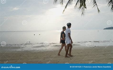 Interracial Couple Walking Holding Hands Along The Sea At A Tropical