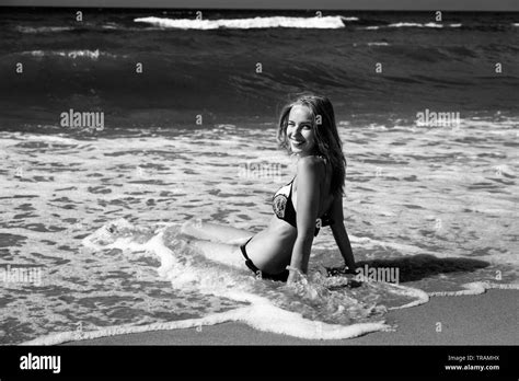 Young Blond Woman In Swimsuit At Sea Surf With Foam Sitting Under Sun Rays Monochrome Looking