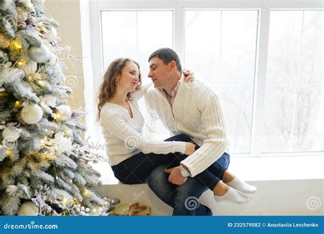Loving Couple In White Cozy Warm Sweaters At Home Near Christmas Tree Smiling Having Fun With