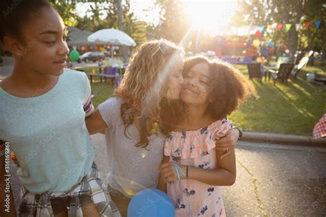 Affectionate Mother Kissing Daughters Cheek At Summer Neighborhood Block Party In Park Stock