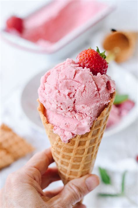 A Hand Holding An Ice Cream Cone With Strawberries On Top