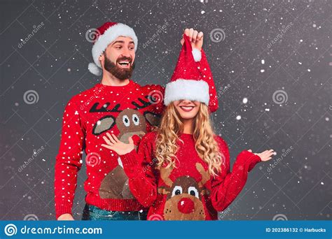 jovencita y divertida pareja en cálidos sudores y sombreros de navidad en fondo gris foto de