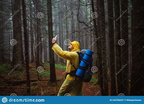 Tourist In A Yellow Jacket Stands In A Dark Rainforest And Catches A