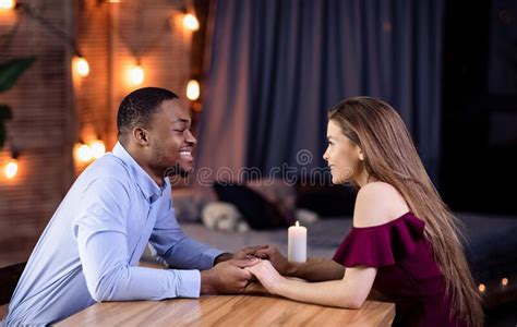 Portrait Of Affectionate Interracial Couple Holding Hands During Romantic Date At Home Stock