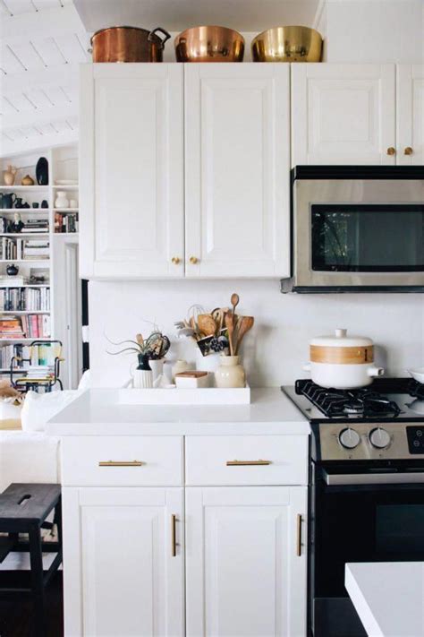 This idea of adding white kitchen cabinets to your kitchen is perfect for someone who wants to add a modern look while keeping it simple. copper and brass cookware above white cabinets with ...