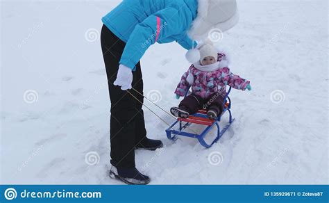 Young Mother Rolls Little Baby On Sled Along Snowy Road In Winter
