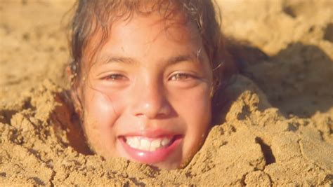 A Young Boy And Girl Smile While They Are Buried In Sand Up To The Neck