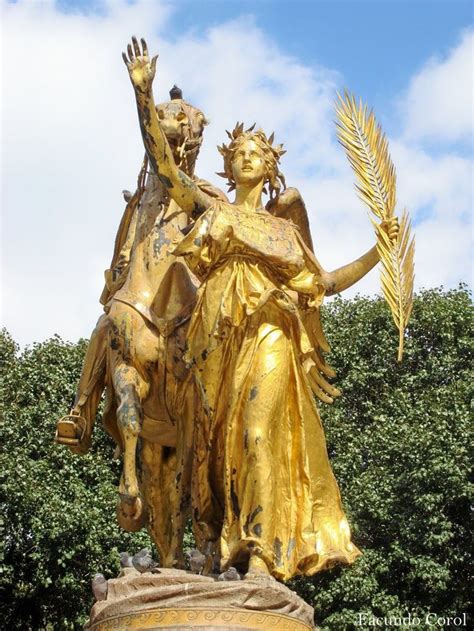 A Golden Statue Holding A Plant In It S Hand And Standing Next To A Tree
