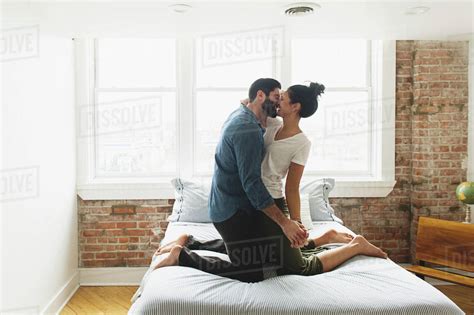 Romantic Couple Kissing While Kneeling On Bed At Home Stock Photo Dissolve