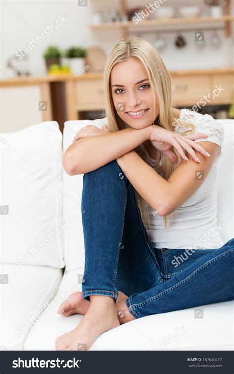 Casual Pretty Young Woman Relaxing At Home Sitting With Her Bare Feet Up On A Sofa Sitting