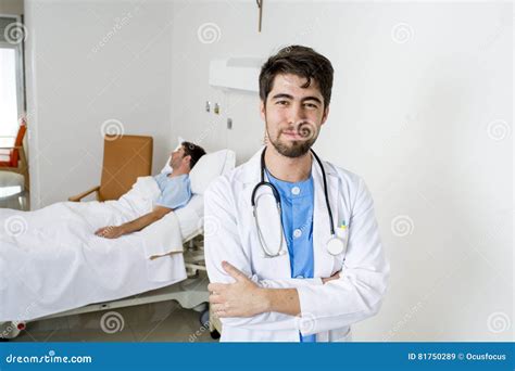 Young Doctor At Hospital Bedroom With Sick Patient Lying In Bed Stock
