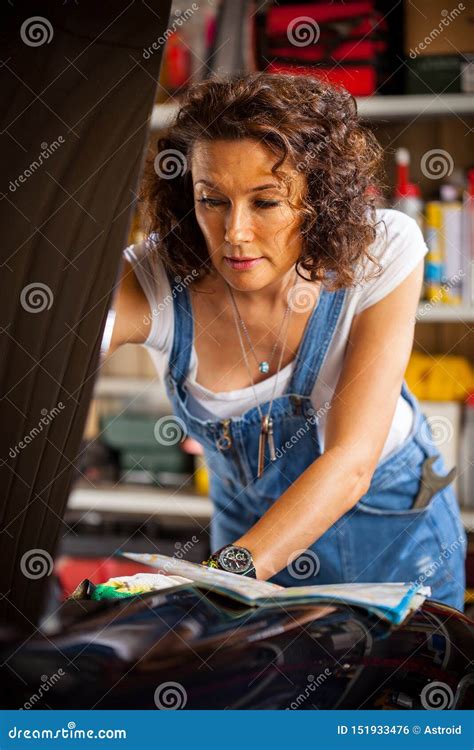 Mechanic Woman In A Blue Coveralls Adjusts The Car`s Engine Stock Photo