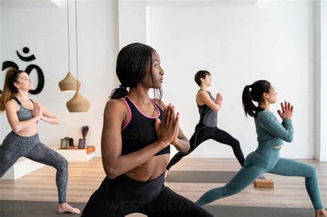 Side View Of African American Woman In Company Of Diverse People Practicing Yoga In Warrior Pose
