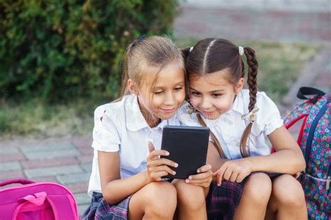 Chicas Jóvenes Que Leen Un Ebook Alumnos De La Escuela Primaria Las Muchachas Con Las Mochilas