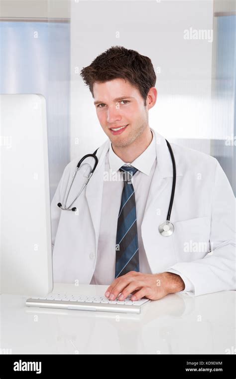 Portrait Of Happy Male Doctor Using Computer At Desk In Clinic Stock