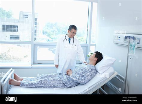 A Doctor Talking To A Patient Lying On The Bed In Hospital Room Stock