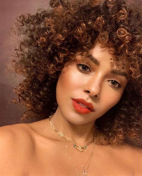 A Close Up Of A Woman With Curly Hair Wearing A Necklace And Red Lipstick On Her Face