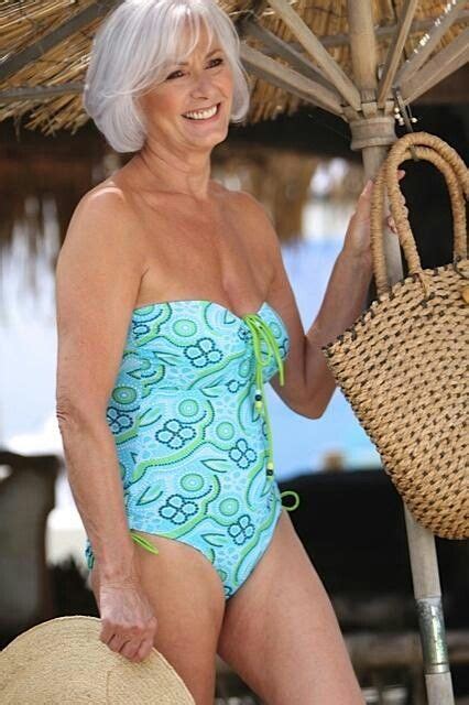 An Older Woman In A Blue And Green Swimsuit Smiles While Sitting Under