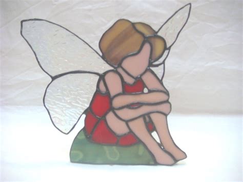 A Stained Glass Figurine Of A Fairy Sitting On Top Of A Green Pillow
