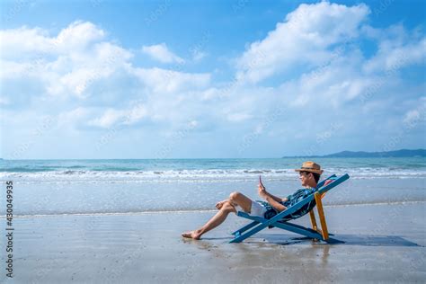 asian man resting on sunbed on tropical beach happy guy sitting on beach chair by the sea using