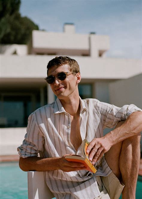 A Man Sitting On The Edge Of A Swimming Pool Wearing Sunglasses And