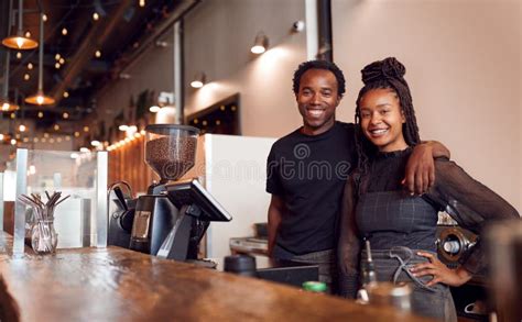 Portrait Of Male And Female Coffee Shop Owners Standing At Sales Desk