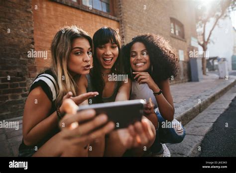Female Friends Sitting Outdoors And Making Selfie With Smart Phone