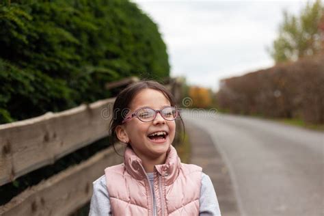 Little Beautiful Cute Girl In Glasses Laughing Near A Wooden Fence
