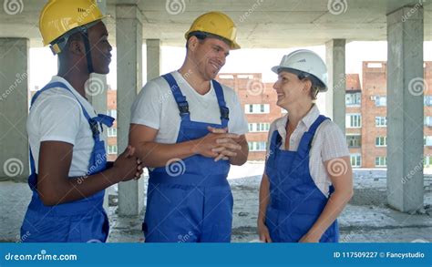 Group Of Smiling Builders In Hardhats Talking At Construction Site