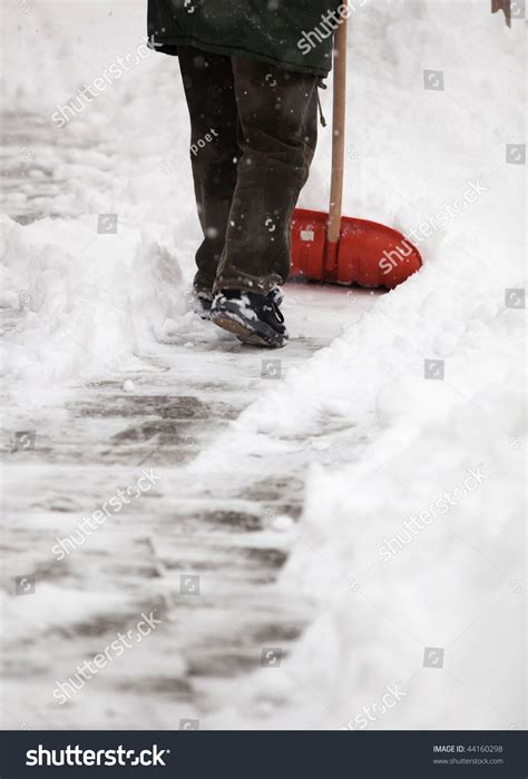 Man Shoveling Snow From The Sidewalk In Front Of His House After A