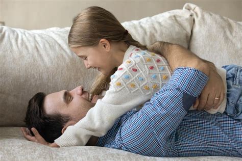 Happy Young Father Cuddling Small Daughter Lying On Sofa Stock Photo