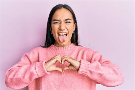 Young Asian Woman Doing Heart Symbol With Hands Sticking Tongue Out