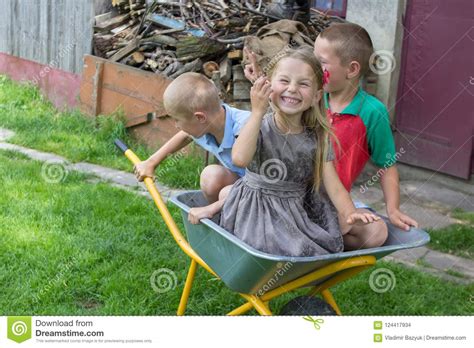 Children Sit In A Wheelbarrowgirl Laughing With Her Brothers Sitting