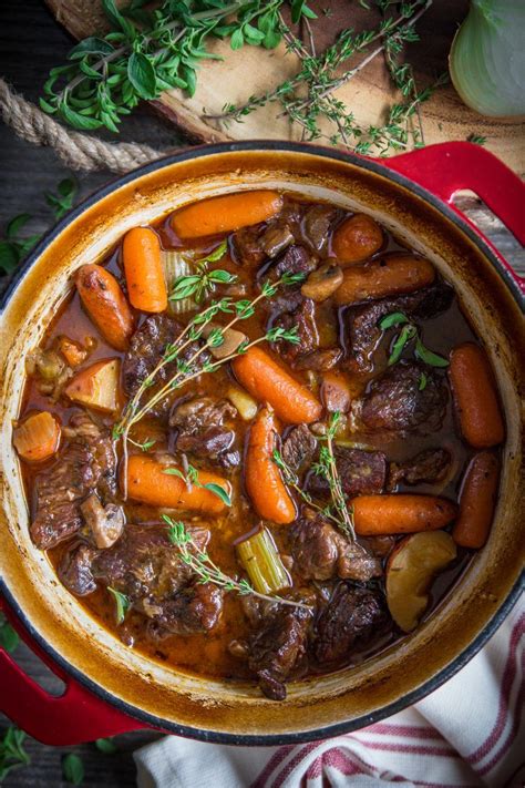 Braised Beef Stew In A Red Dutch Oven Pot With Herbs Beside It Dutch