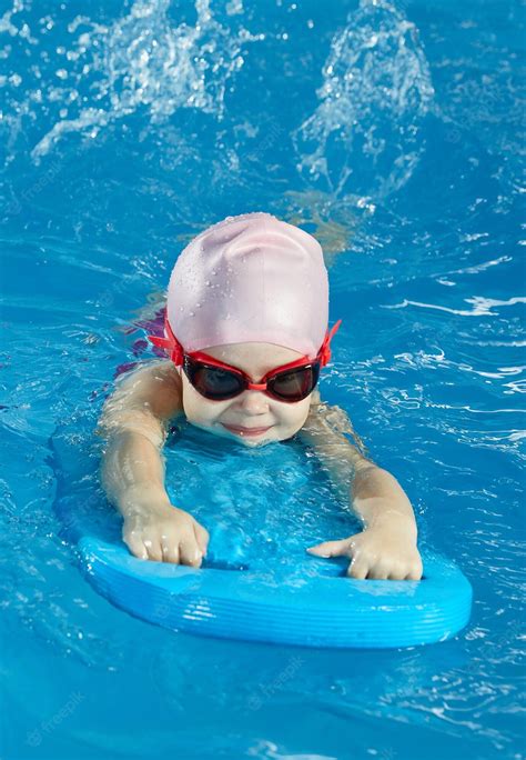 Маленькая девочка учится плавать в крытом бассейне с доской для