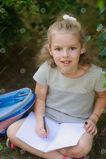 Little Schoolgirl Sits Having Crossed Legs Under A Tree And Holds On