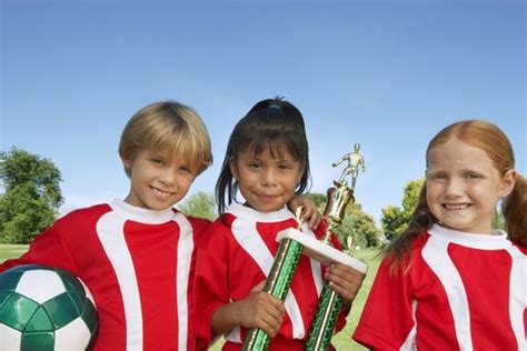 Portrait Of Children Soccer Team Holding Ball And Trophy On Field By