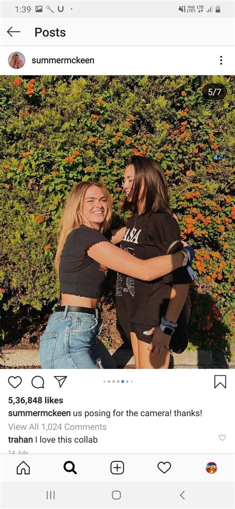 Two Girls Hugging Each Other In Front Of Some Bushes