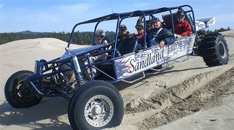 A Group Of People Riding In The Back Of A Buggy On Top Of Sand Dunes