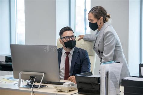 Young Businesswoman And Her Colleague In Masks Computing And