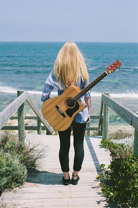 Girl With A Guitar On Her Back Stands And Looks At The Ocean By