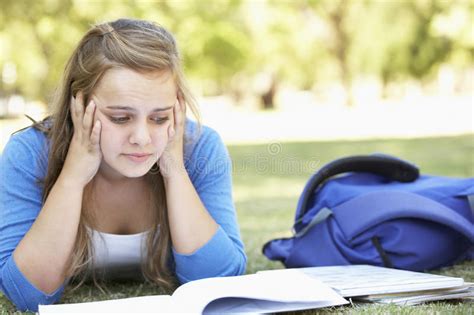 Female College Student Lying In Park Reading Textbook Stock Photo