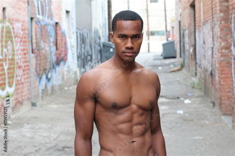 Under The Sunshine A Masculine Black Guy Half Naked Is Standing By An Alley With Rough