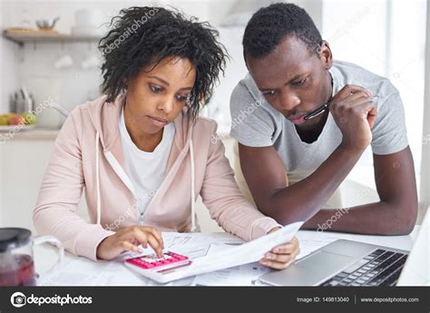 Stressed African American Couple Working Through Paperwork Together Calculating Expenses