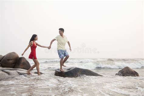 Young Couple Standing And Holding Hands On The Beach And Looking Out To