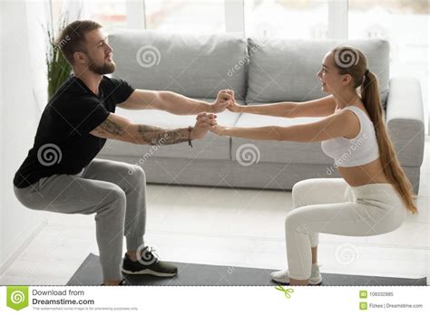 Young Sporty Couple Doing Squats Holding Hands Together At Home Stock