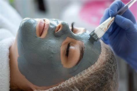 Hands Of Beautician Applying Beauty Mask On Young Woman Face At
